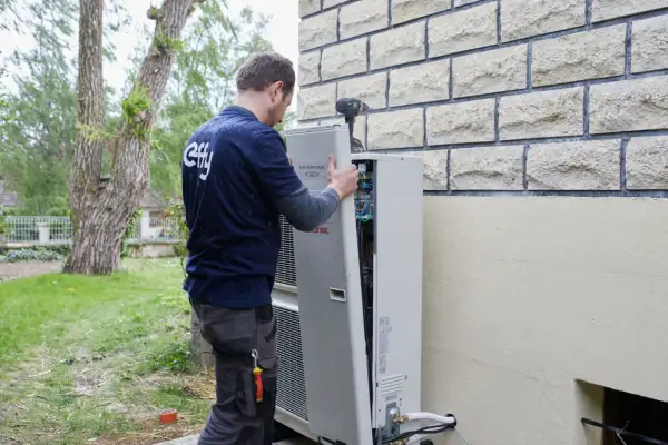 Un technicien installe une pompe à chaleur. La distance avec la maison du voisin est prise en compte pour le bruit.