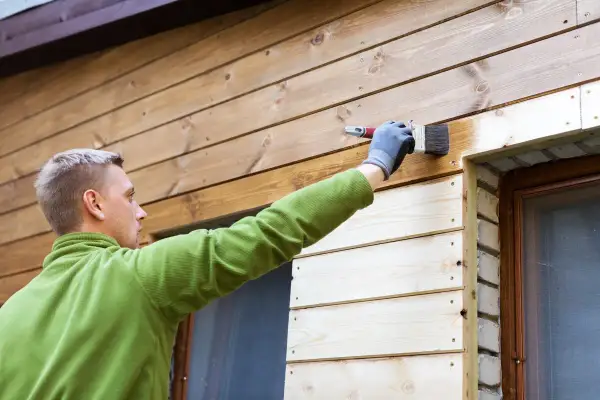 Man målar panel utomhus med en pensel. Träet är ljust och fräscht.