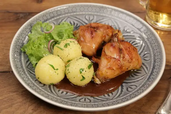 Saftiger Hasenbraten Hausfrauenart mit Klößen, Salat und dunkler Soße auf einem gemusterten Teller.