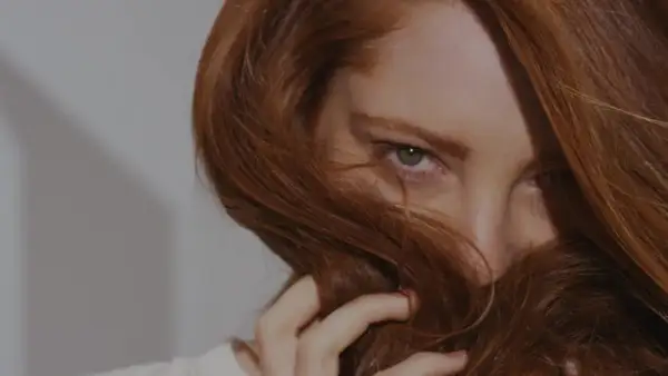 Occhi penetranti emergono da una cascata di capelli ramati, un invito a scoprire come fare il rosso scuro perfetto.