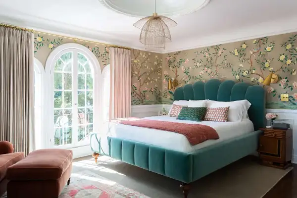 Chinoiserie wallpaper with birds and blossoms offers stunning bedroom wall decor ideas. A teal velvet bed and pink curtains complete the elegant look.