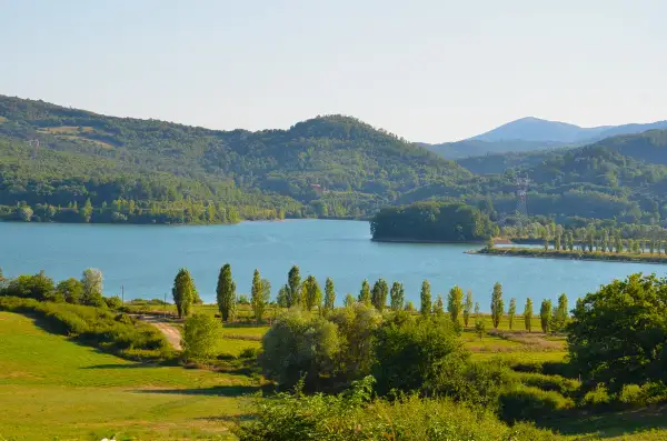 Vasta distesa azzurra del lago di Bilancino, circondata da dolci colline verdi e alberi rigogliosi sotto un cielo limpido.