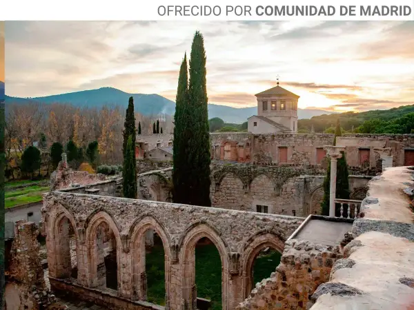Ruinas de antiguos monasterios cerca de Madrid, con arcos de piedra y cipreses altos bajo un cielo crepuscular.
