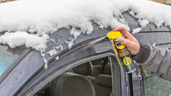 Hand sprüht Silikonspray auf die Gummidichtung des Autos, um sie vor Frost zu schützen und die Gummidichtung zu reparieren.