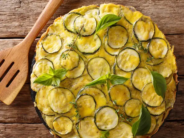Une délicieuse scarpaccia de courgettes, garnie de basilic frais et de thym, prête à être servie avec une spatule en bois.