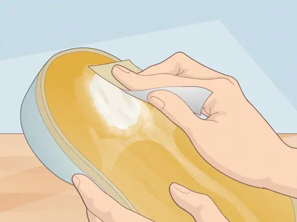 Préparation d'une semelle de chaussure pour la recoller sans colle. Une main frotte la surface avec un papier abrasif.