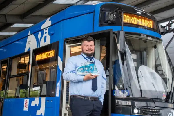 Pracownik MPK trzymający model tramwaju przed niebieskim pojazdem. To symbol publiczny transport krakow.