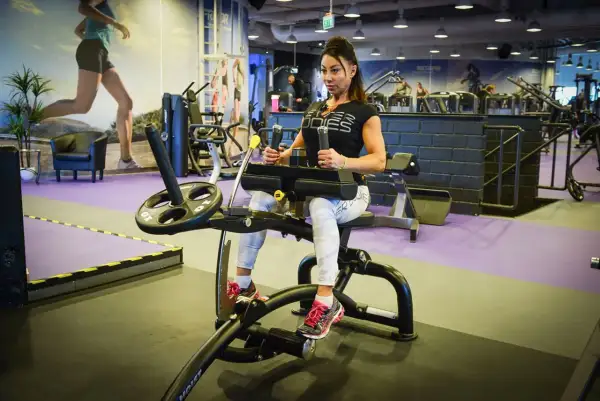 Kvinna tränar magen på gymmaskin. Hon har på sig träningskläder och fokuserar på sin vad press.