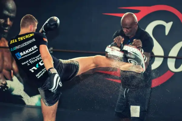 En fighter sparkar mot en träningspad som hålls av en tränare. Kanske en träning med Ernesto Hoost?