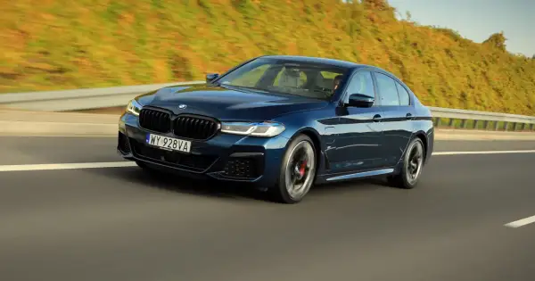 Ciemnoniebieskie BMW 545e pędzi autostradą, otoczone zielenią.
