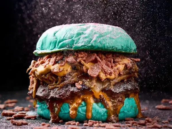 Una hamburguesa gigante con pan azul, carne jugosa, queso derretido y crujiente tocino, perfecta para un festival hamburguesa.