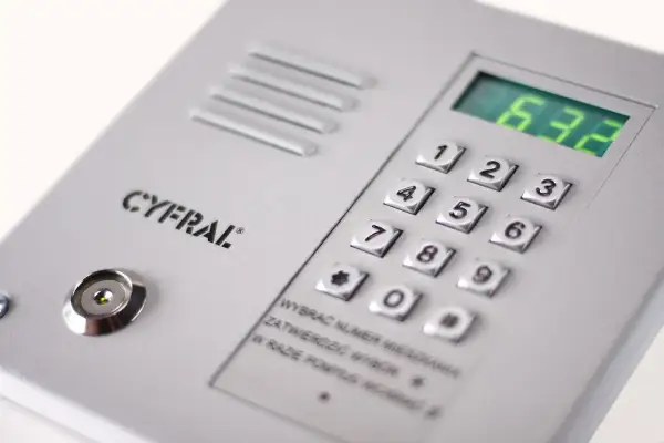 Panel domofonu Cyfral z klawiaturą numeryczną i wyświetlaczem. Instrukcja podpowiada, jak ściszyć domofon, wybierając numer mieszkania i potwierdzając go.