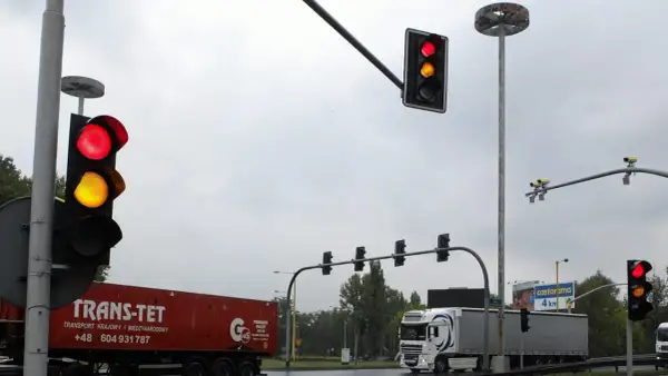 Na skrzyżowaniu widać czerwone i żółte światła. Białe kamery nad światłami monitorują ruch.