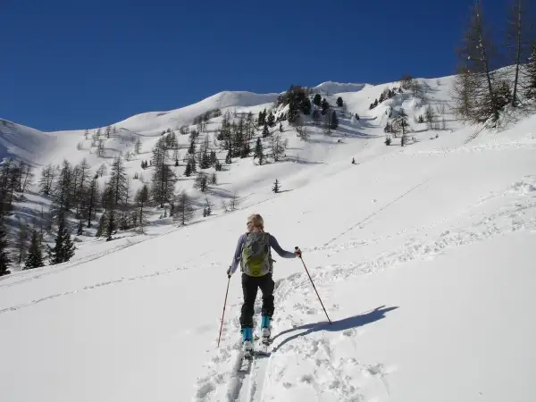 Sciatrice con zaino e bastoncini, in un paesaggio innevato con alberi radi e montagne sullo sfondo. La **forca canapine** è il suo obiettivo.