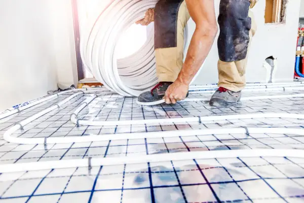 Worker installing underfloor heating pipes on a grid system.
