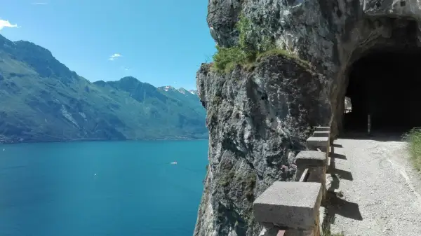 Sentiero panoramico per trekking a Riva del Garda, con vista sul lago e un tunnel scavato nella roccia.