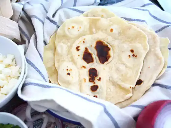 Färska tortillabröd, perfekta för ditt nästa tortilla recept. Bredvid syns skålar med tillbehör som ost och lök.
