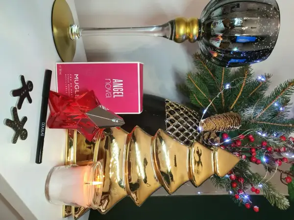 Świąteczna kompozycja z perfumami Angel Nova Mugler 50 ml, świecą, choinką i ozdobami.