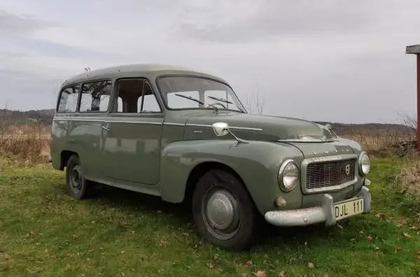 Grön Volvo P210 parkerad på en gräsmatta. Bilen har en klassisk design och ser ut att vara i gott skick.