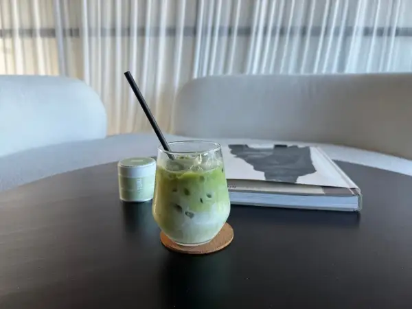 Un verre de lait matcha glacé, parfait pour profiter des bienfaits du matcha. Une petite boîte de matcha est à côté.