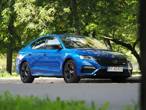 Błękitna Skoda Octavia RS 2025 z czarnymi felgami, zaparkowana wśród zieleni.