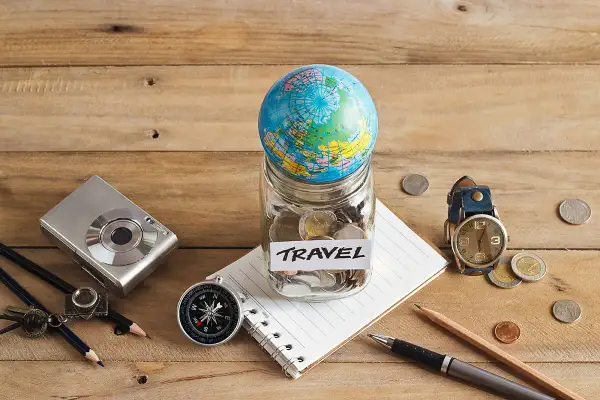 Bocal rempli de pièces avec un globe, un appareil photo, une boussole et un carnet, prêt pour le backpacking en Europe.