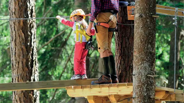 Bambina con casco giallo e adulto su passerella in un parco avventura Marche.