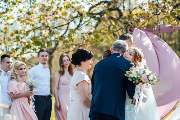 Nowoczesne błogosławieństwo: panna młoda tuli ojca, podczas gdy rodzina i świadkowie obserwują wzruszającą chwilę.