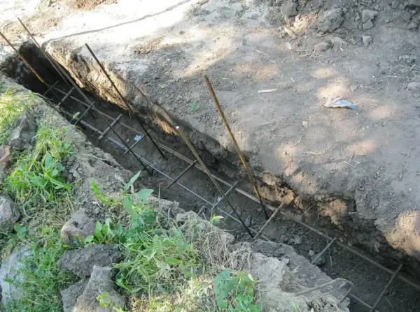 Zbrojenie do fundamentu ogrodzeniowego w wykopie. Metalowe pręty tworzą siatkę, gotową na zalanie betonem.