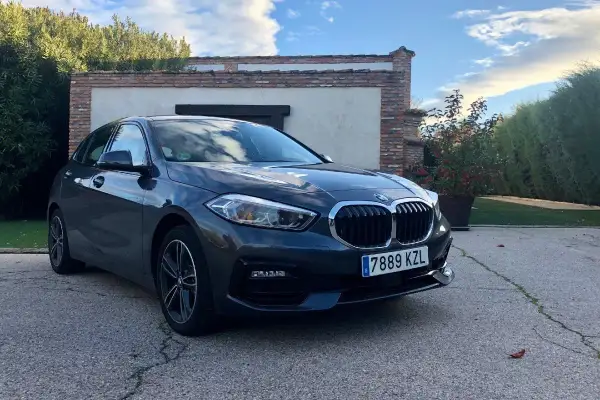 Un BMW Serie 1 116d gris aparcado frente a una casa con vegetación. A pesar de su aspecto, este modelo puede presentar problemas.