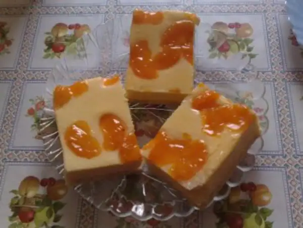Drei Stücke faule weiber kuchen mit Mandarinen auf einem Tisch mit Blumenmuster.