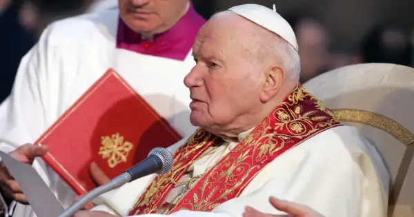Papież Jan Paweł II podczas modlitwy do Ducha Świętego o uzdrowienie. W rękach trzyma dokument i czerwoną księgę.