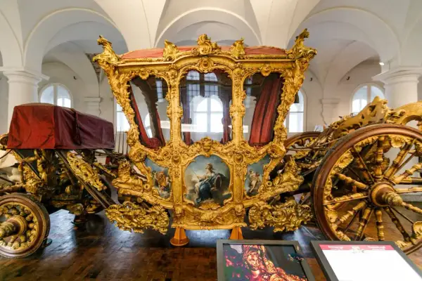 Prunkvolle Kutsche im Marstall Museum, vergoldet und mit Gemälden verziert, ein Zeugnis vergangener Pracht.