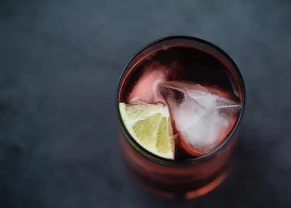 Szklanka z ciemnym napojem, lodem i plasterkiem limonki. Idealny drink z Asbach Uralt, by poczuć smak lata.