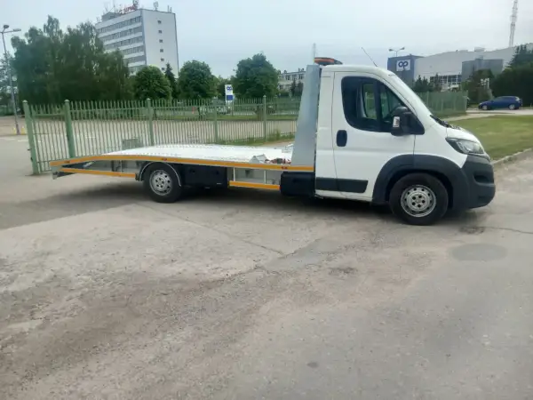 Biała laweta z platformą stoi na placu. Zastanawiasz się, ile kosztuje laweta?