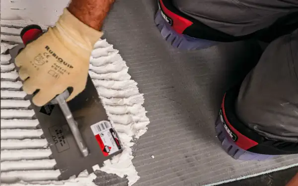 Pose d'enduit avec une truelle crantée pour le carrelage. Le choix du bon taille peigne carrelage est essentiel pour une pose parfaite.