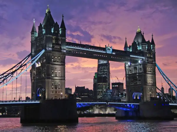 Wieczorny widok na Tower Bridge, jeden z najpiękniejszych zabytków w Londynie, z fioletowym niebem w tle.