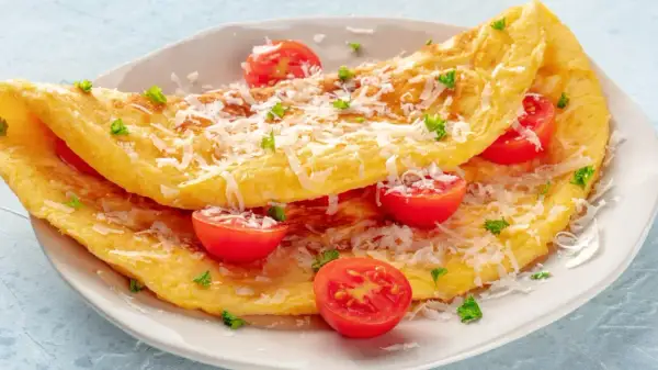 Puszysty omlet z serka wiejskiego, posypany parmezanem i udekorowany pomidorkami koktajlowymi i natką pietruszki.