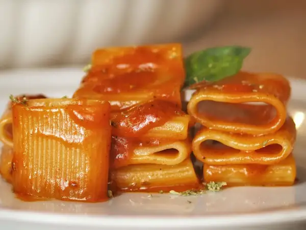 Piatto di pasta allo scarpariello, con rigatoni conditi da un sugo rosso e guarniti con basilico fresco.
