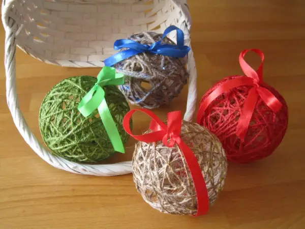 Palline decorative fatte con spago e colla vinilica, decorate con nastri colorati, appoggiate vicino a un cestino bianco.