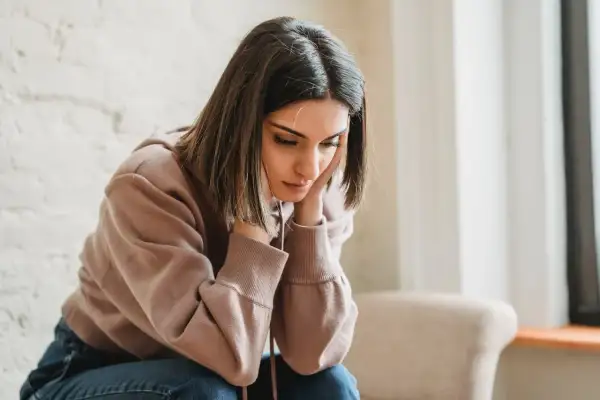 Una joven con las manos en la cara, con expresión de tristeza, parece reflexionar sobre qué es ser pesimista.