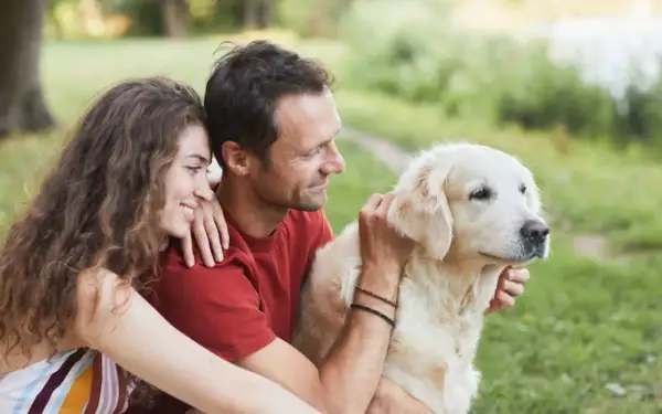 Un couple câlinant leur chien doré en plein air. Ils semblent réfléchir à comment faire garder son chien pour leurs prochaines vacances.