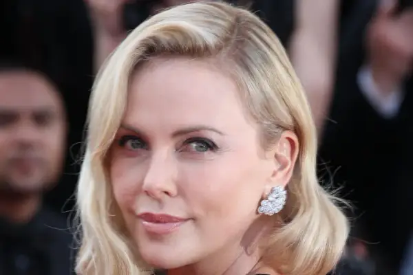 Charlize Theron mit eleganten Frisuren mit Wirbel am Hinterkopf, glitzernden Ohrringen und einem strahlenden Lächeln.
