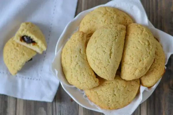 Dolci tipici bologna: biscotti dorati ripieni di marmellata, serviti in una ciotola bianca su un tovagliolo.