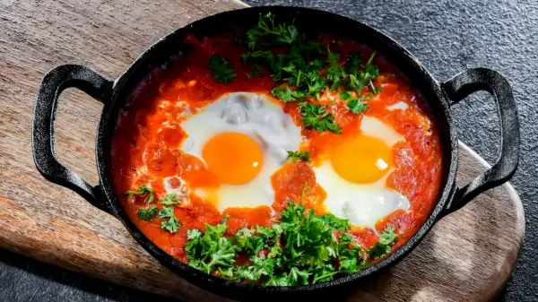 Herzhaftes Shakshuka-Rezept: Eier in würziger Tomatensoße, garniert mit frischer Petersilie, serviert in einer Gusseisenpfanne.