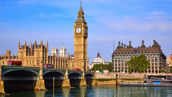 Big Ben Londyn z czerwonymi autobusami na moście i rzeką w tle.