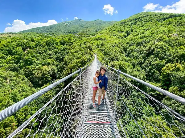 Bambini su un percorso ponte tibetano, circondati da una lussureggiante foresta verde sotto un cielo azzurro.
