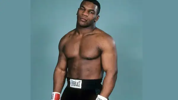 Mike Tyson's powerful physique is on full display, showcasing his legendary mike tyson abs and muscular chest. He wears boxing shorts and gloves.