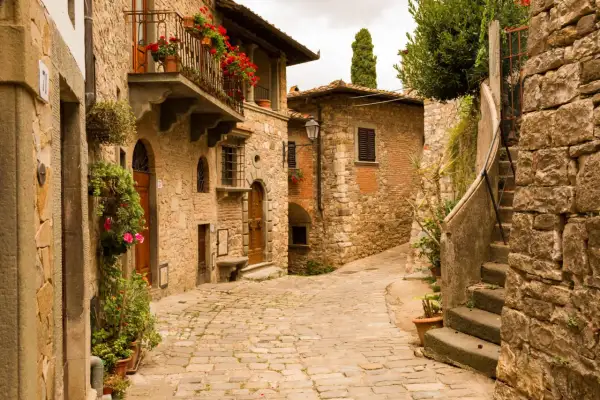 Un vicolo acciottolato tra antichi borghi toscani poco conosciuti, con case in pietra, balconi fioriti e un'atmosfera senza tempo.