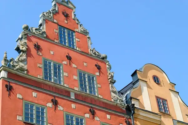 Fasaderna på ett gammalt hus i Stockholm, som en gång kan ha varit ett slott eller värdshus, med detaljerad utsmyckning och röda och gula färger mot en blå himmel.